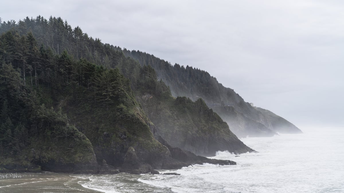 Moody coastal cliffs and hills jut out into the Pacific Ocean as seen from the Hacienda Lighthouse in Oregon